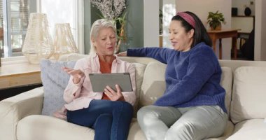 Çeşitli bayan arkadaşlar tableti tıkırdatıyor, içeriği gösteriyor, oturma odasında işaret ediyor ve gülüyorlar. Yaşam tarzı, bağlantı, iletişim, konforlu, konuşkan, modern, boş zaman