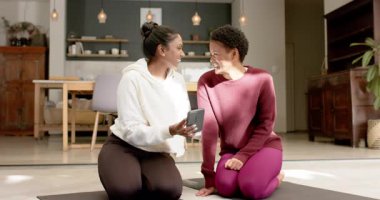 Evde yoga minderleri üzerinde diz çöküp telefonları işaret eden, gülen, yoga hazırlayan çeşitli bayan arkadaşlar. Refah, dostluk, rahatlama, dostluk, gündelik, samimi, modern