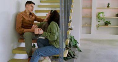 Bir çift kahve fincanı tutuyor ve merdivenlerde eşlerine gülümseyen adamlardan sonra parmaklarını kilitliyor. Romantizm, samimiyet, bağlantı, rahatlama, modern, samimi, yaşam tarzı