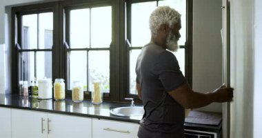 Afro-Amerikalı adam buzdolabından süt alıyor, pudranın yanına yerleştiriyor, meyve suyu için muz soyuyordu. Sağlık, fitness, beslenme, modern, sağlık, yemek pişirme, yaşam tarzı