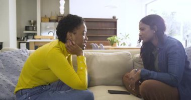 Evde oturan çeşitli bayan arkadaşlar ellerinde akıllı telefon olan sarı elbiseli bir kadının jestine gülüyorlar. Gündelik, dostluk, iletişim, sıcaklık, modern, rahatlama, iç mekan