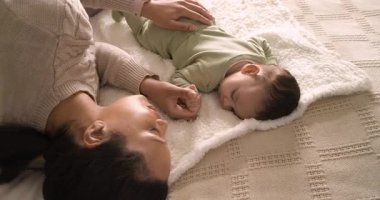 Anne akıllı bir şekilde küçük kızı okşuyor ve battaniyenin üzerinde elini tutuyor. Şefkat, bakım, aile içi, rahat, bağlantı, uyku, sükunet