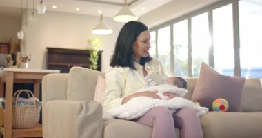 Anne oturma odasına giriyor, yeni doğmuş bebeği beyaz bir battaniyeyle kanepede sallıyor ve bebeği sakinleştiriyor. İlgi, bağ, şefkat, sükunet, ev, rahatlık, bakım