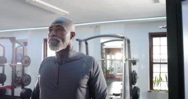 Kıdemli Afro-Amerikan adam spor salonundaki çömelme yerlerini tarıyor, göğüs göğüse geçiyor ve kendine güveniyor. Zindelik, güç, kararlılık, sağlık, canlılık, egzersiz, çağdaş