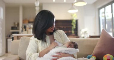 Anne karnını doyurmak için bebeği göğsüne kaldırırken kafasını okşuyor, pencerenin yanındaki koltuğa oturuyor. Ebeveynlik, yetiştirme, yakınlık, rahatlık, minimalist, samimi, aile