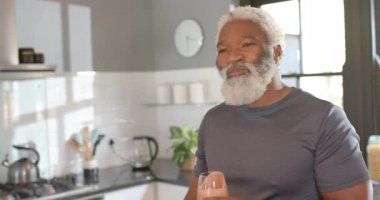 Kıdemli Afrikalı Amerikalı adam aroma soluyor, açık mutfakta smoothie yudumluyor lezzet değerlendirmesi yapıyor. Sağlıklı, sağlıklı, yaşam tarzı, çağdaş, canlılık, rahatlama, beslenme