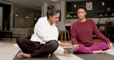 Çeşitli bayan arkadaşlar yoga minderlerindeki akıllı telefonu ayarlarken evdeki ısınma akışına rehberlik ediyorlar. Sağlık, farkındalık, dostluk, egzersiz, rahatlama, modern, dingin