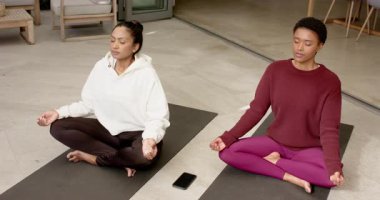 Çeşitli bayan arkadaşlar stüdyodaki yoga minderlerine odaklanmak için akıllı telefonlarıyla meditasyona giriyorlar. Meditasyon, farkındalık, dinginlik, refah, dostluk, iç mekan, huzur