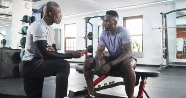 Afrika kökenli Amerikalı antrenör ve stajyer egzersiz öncesi spor salonundaki telefon çalışma planını gözden geçiriyorlar. Kişisel eğitim, spor, güç, motivasyon, koçluk, halter, beden eğitimi.