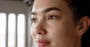 Yirmili yaşlarda bir kadın pencereden dışarı bakıyor, yavaşça göz kırpıyor ve gülümsüyor. Düşünce, sükunet, doğal ışık, içgözlem, samimiyet, duygu, minimalizm