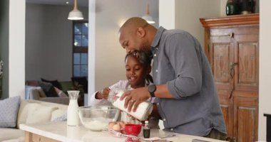 Afrika kökenli Amerikalı baba ve kız ellerinde kavanoz, un ve sütü kâseye doldurup hamuru yapıyorlar. Aile, kaynaşma, mutfak, yemek pişirme, oyuncu, birliktelik, aile içi ilişkiler.