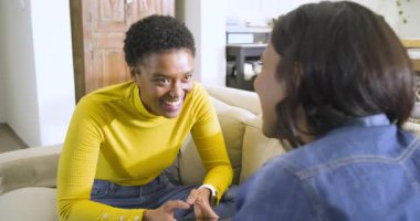 Başını sallayarak, Afrikalı Amerikalı ve Hintli arkadaşlar bej kanepede telefon fotoğraflarını paylaşıyorlar. Arkadaşlık, iletişim, sosyalleşme, gündelik, rahat, modern, yaşam tarzı