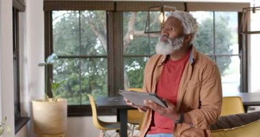 Oturma odasına giriliyor, yetişkin Afro-Amerikalı bir adam vitrinde tablet kaydırıyor ve içeriği gözden geçiriyor. Teknoloji, yaşam tarzı, modern, rahatlama, iç mekan, konsantrasyon, iletişim