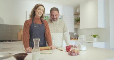 Bir çift fırında pişirme, merdaneli hamuru yuvarlama ve mutfak adasından bardak alma konusunda şakalaşıyor. Aşçılık, mutfak, ev yapımı, aşçılık, takım çalışması, konforlu, yaşam tarzı