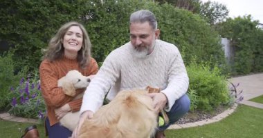 Kıdemli çift çimlerin kenarında diz çöküp kıvranan köpek yavrusu tutarak yaşlı köpekleri okşuyor. Evcil hayvanlar, arkadaşlık, açık hava, rahatlama, arkadaşlık, kırsal, iç açıcı