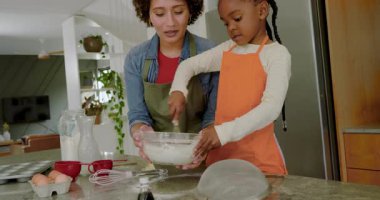 Çeşitli anne ve kız unları ölçüyor sonra hamuru mutfak adasında çırpıcıyla karıştırıyor. Aşçılık, aile, eğitim, yetiştirme, işbirliği, sıcak, çağdaş