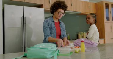 Anne ve kızı mutfak adasında ekmek ve havuç dilimliyor öğle yemeklerini sırt çantasında sarılıyorlar. Aile, yemek hazırlığı, yetiştirme, eğitim, yerli, samimi, kırsal