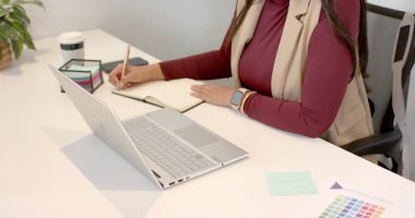 Defteri açmakla başlayan kadın, gümüş dizüstü bilgisayarın yanında gül sarısı kalemle yazıyor. Profesyonel, çalışma alanı, modern, üretkenlik, yaratıcılık, odaklanma, durağanlık