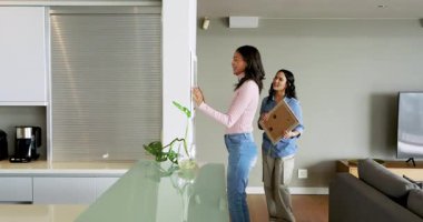 Çeşitli bayan arkadaşlar oturma odasında şarap kadehi ve saksı bitkisiyle çerçeveli resim asıyorlar. İç mekan, işbirliği, çağdaş, rahatlama, ev, tasarım, yaşam tarzı