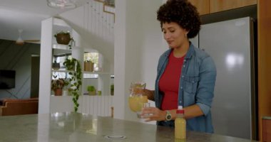 Anne buzdolabı açıyor, meyve suyu dolduruyor, Afrika kökenli Amerikalı kızın ödev yapmasına yardım ediyor. Aile, yerli, ev, yetiştirme, eğitim, sağlıklı yaşam tarzı, modern iç mimari