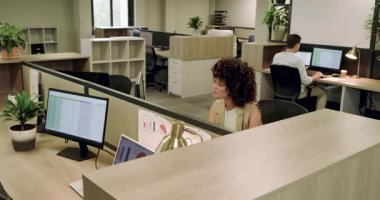 Çift monitörlerdeki hesap tablolarını inceleyen ve açık planlı ofiste geri bildirim paylaşan çeşitli iş arkadaşları. İşbirliği, takım çalışması, modernlik, teknoloji, iletişim, üretken, profesyonel