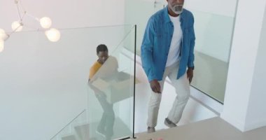 Afro-Amerikalı baba ve oğul kanepenin üzerindeki kutuları boşaltıp çerçeveli fotoğraf çektiriyorlar. Aile, yer değiştirme, ev yenileme, modern iç mimari, miras, bağ, yeni bir başlangıç.