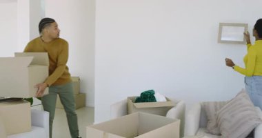 Taşınan kutuları açarak, farklı çiftler boş oturma odasının duvarına resim çerçevelerini diziyorlar. Ev dekorasyonu, takım çalışması, yenileme, iç tasarım, yaşam tarzı, çağdaş, estetik