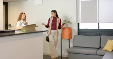 Bir kadın lobiye giriyor, resepsiyonistle sohbet ediyor, sonra da akıllı telefonuyla kanepeye yürüyor. Profesyonel, işbirliği, modern, işyeri, gayri resmi, iletişim, takım çalışması