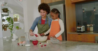 Çeşitli anne ve kızları mutfak adasında kâsede karıştırıyor ve sütü döktükten sonra kaşıkla hamuru pişiriyorlar. Aile, yemek pişirme, mutfak, bağ, sıcaklık, ev işleri.