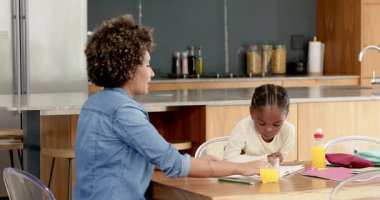 Anne, meyve suyu bardağının yanındaki mutfak masasında kızının eline rehberlik ediyor. Aile, eğitim, bağlanma, akıl hocalığı, yerli, yetiştirme, öğrenme