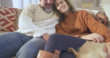 Kucağında köpek yavrusu uyuyan ve kanepede sevişen süveter giyen romantik çift. Şefkat, samimiyet, arkadaşlık, rahatlama, evcil, samimi, hassas