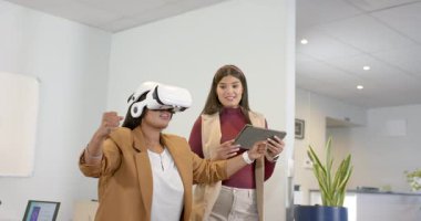Çeşitli meslektaşlar, VR simülasyonunu başlatan tablete dokunuyor, kulaklık takan kadın ofise ulaşıyor. Gelecekçi, yenilikçi, işbirliği, teknoloji, dalgın, profesyonel, dinamik
