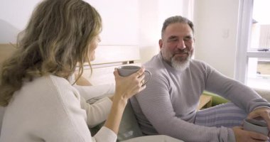 Son sınıf çifti gülümsemelerini yudumluyor evde fincan yudumluyor gülüşlerini paylaşıyor destekleyici konuşmalara geçiyorlar. Samimiyet, samimiyet, rahatlama, duygusal bağlantı, aile sakinliği, içten, sevecen.