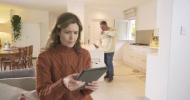 Tabletteki uyarı, mutfaktan kanepeye yürüyen ve tebligatı gözden geçiren çift. Modern, samimi, işbirlikçi, dijital, yaşam tarzı, ev, etkileşim