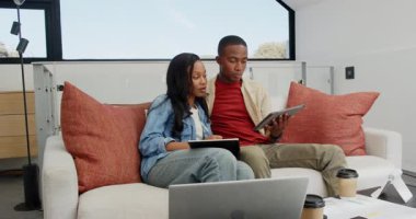 Kanepe planlama projesinde oturan siyah bir çift kahve fincanı alıp tabletteki tablolara işaret ediyorlar. İşbirliği, takım çalışması, modern, yaşam tarzı, odaklanma, iletişim, yenilik