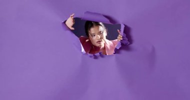 Pembe ceketli Asyalı kadın mor kağıtları kırıyor, kararlı görünüyor. Güven, güç, atılım, hırs, iş, moda.