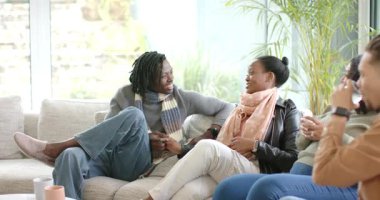 Farklı arkadaşlar sohbete dalarken Rastalı adam oturma odasında kanepeye eğilip konuşuyor. Arkadaşlar, sosyalleşme, gündelik, modern, canlı, bağlantı, rahatlama