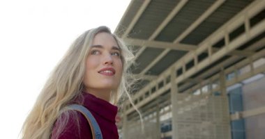 Şehir merkezinde metal bir gölgeliğin altında yürüyen, saçları tarayan ve kot çantalı bir kadın. Kentsel, yaşam tarzı, minimalizm, moda, ilham, keşif, mimari