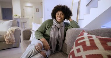 Kanepeye bakan, saçları tarayan, gülen, kameraya bakan bir kadın. Modern, yaşam tarzı, samimi, samimi, dost canlısı, rahat, iç mekan