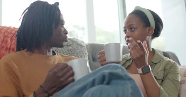 Afro-Amerikalı kadınlar, kanepede rahat etmek için birbirlerine bakıyorlar, el kol hareketi yapıyorlar ve sarılıyorlar. Samimiyet, bağlantı, rahatlama, samimiyet, dostluk, samimiyet, sevgi