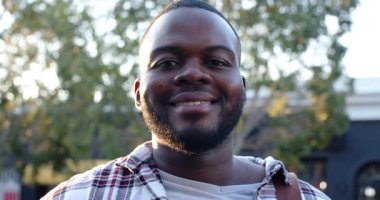 Sokakta kahverengi çantalı Afro-Amerikalı adam kameradan gülümseme ve kahkahalara yanıt veriyor. Portre, sokak giysisi, samimi, enerjik, canlı, açık hava, boş zaman