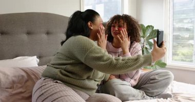 Anne ve kızı, pembe bantlar takarken akıllı telefon kullanarak yatakta kayıt yapıyorlar. Cilt bakımı, aile, bağ kurma, rahatlama, rahatlama, rahat, doğal