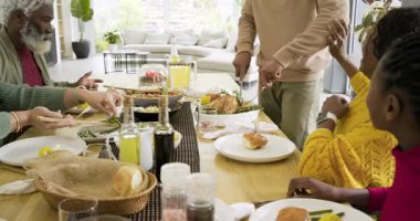 Orta yaşlı Afro-Amerikan bir adam yemek masasında yemek servisi yaparken bıçağı kapıp hindiyi dilimliyor. Aile, toplanma, kutlama, kırsal, sıcak, neşeli, neşeli