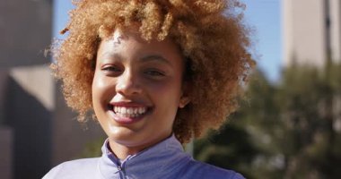 Afrika kökenli Amerikalı kadın güneş ışığı alıyor ve gülümsüyor başını eğiyor ve çatı çekimine gülüyor. Neşe, mutluluk, canlılık, açık hava, moda, anlamlı, enerjik