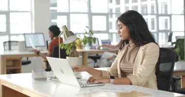 Akıllı telefonlara ulaşmadan önce spor ceketli Hintli kadın dizüstü bilgisayar ve çizelge kullanıyor. Profesyonel, işbirlikçi, modern, teknoloji, çoklu görev, üretkenlik, kurumsal