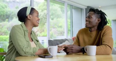 Konuşurken el ele tutuşan ve derin bir bağ kurmak için evlerinde kupa yudumlayan Afro-Amerikalı çift. Samimiyet, arkadaşlık, sıcaklık, iletişim, rahatlama, samimi, samimi.