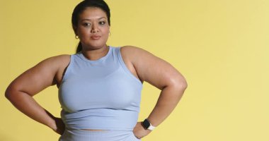 Aktif giysili kadın sarı arka plana karşı modellik yapmak için geriye doğru bakıyor. Fitness, activewear, kendinden emin, kararlı, stüdyo, sadelik, yaşam tarzı