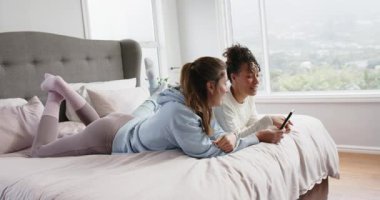 Yatakta uzanmış çeşitli bayan arkadaşlar akıllı telefon ekranlarını dinliyorlar, komik içeriği gösteriyorlar, gülüyorlar. Gündelik, arkadaşlık, rahatlama, modern, rahat, boş zaman, teknoloji