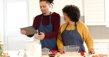 Yemek pişiren çift, yemek tarifi uyarısı tableti görüyor, talimatları kaydırıyor ve hamburgeri tezgahta hazırlıyor. İşbirliği, aile, modern mutfak, tarif, teknoloji, ilham, ev hayatı