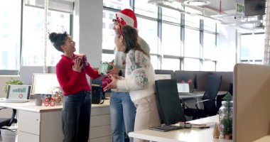 Üç ofis çalışanı, hediyelerini açmak ve hediyelerini denetlemek için masalarda hediyelerini değiştiriyor. Şenlik, dostluk, kutlama, modern, takım çalışması, neşeli, tatil
